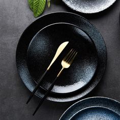 two black plates with gold forks and silverware next to each other on a table