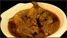 a white bowl filled with meat and gravy on top of a black table