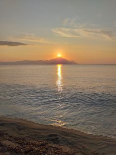 the sun is setting over the ocean with mountains in the distance and water on the shore