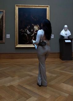 a woman standing in front of a painting and looking at the ground with her back to the camera