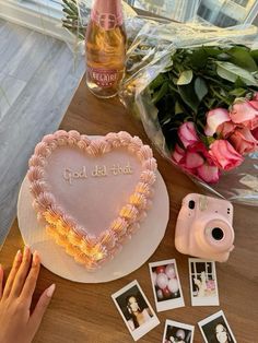 a heart shaped cake sitting on top of a wooden table next to flowers and pictures