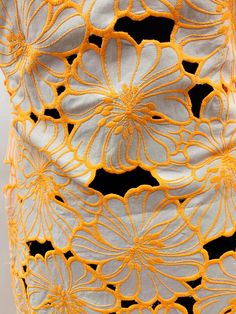 an orange and white crocheted dress with flowers on the bottom, in front of a black background