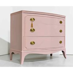 a pink chest of drawers with gold handles and knobs on the top, against a white wall