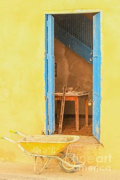 a wheelbarrow sitting in front of a yellow building with blue door and window