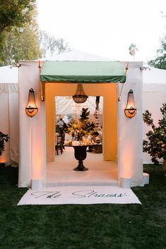 a white tent with green canopy and lights on the front door is set up for an outdoor event