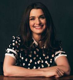 a smiling woman sitting at a table with her arms crossed and looking off to the side