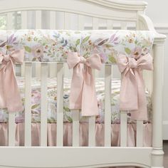 a white crib with pink bows and flowers on the bedding is shown in this image