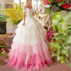 a woman in a white and pink wedding dress standing next to flowers with her hands on her hips