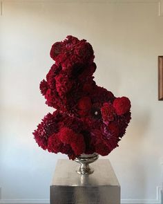 a silver vase filled with red flowers on top of a wooden table next to a white wall