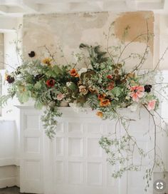 a white fireplace with flowers and greenery on it