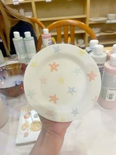 a person is holding up a plate with starfish designs on it and other crafting supplies in the background