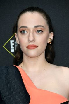 a woman in an orange and black dress posing for the camera with her hand on her hip