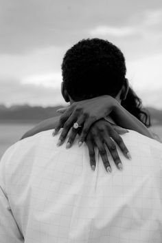 two people embracing each other in front of a body of water