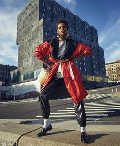 a man standing in front of a tall building wearing a red jacket and black pants