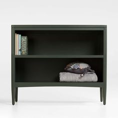 a green bookcase with two books on top of it and some folded blankets in front of it