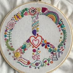 an embroidered peace sign with flowers and hearts in the center on a white cloth background