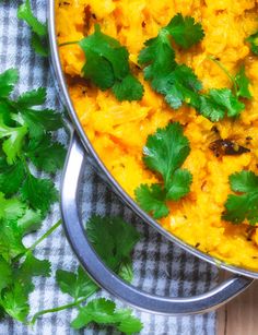 a pot filled with yellow rice and cilantro on top of a checkered cloth