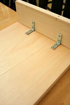 a wooden table with two metal brackets on the top and one is holding a piece of wood