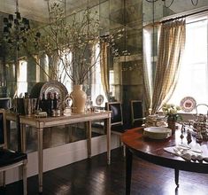 a dining room table and chairs in front of a mirror wall with vases on it