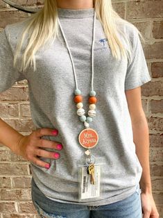 a woman wearing a necklace with an orange and white bead on it, standing in front of a brick wall