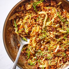 a pan filled with meat and vegetables on top of a white countertop next to a silver spoon