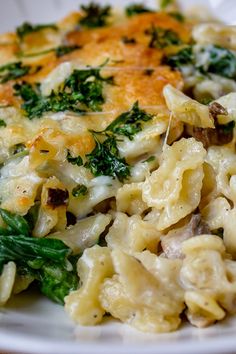 a white plate topped with pasta covered in cheese and spinach toppings on top of a wooden table