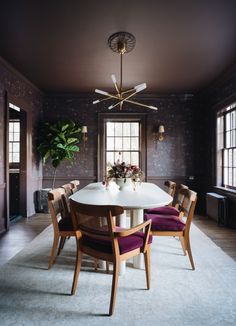 a dining room table with purple chairs and a plant in the center is surrounded by dark wallpaper