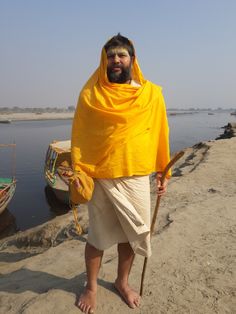 a man wearing a yellow shawl and holding a stick by the water's edge