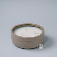 a white candle is sitting in a small bowl on a table with a gray background