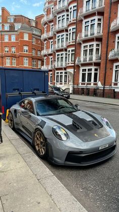 a grey sports car parked on the side of a road next to a blue dumpster