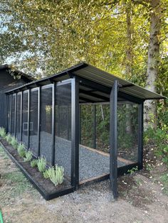 an outdoor shelter with plants growing out of the sides and windows on the side, in front of some trees