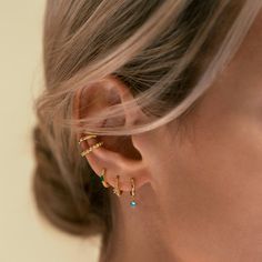 a close up of a woman's ear wearing gold earrings with small green and blue stones