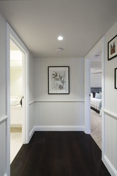 an empty room with wood floors and white walls, framed pictures on the wall above it