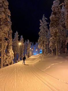 a person skiing down a snow covered hill at night time with trees in the background