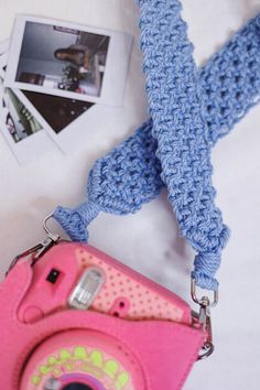 a pink camera sitting on top of a white bed next to a blue crocheted scarf