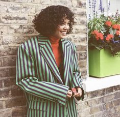 a woman standing next to a brick wall wearing a green and blue striped suit with black stripes