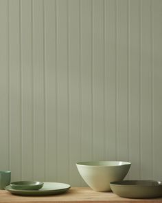 bowls and plates are sitting on a wooden table in front of a wall with vertical stripes