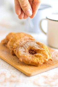 a person is sprinkling sugar on two doughnuts that are on a cutting board