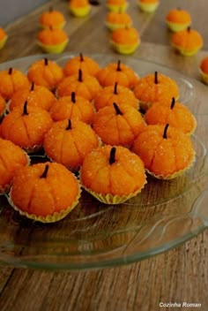 there are many orange cupcakes on the glass plate with black sticks sticking out of them