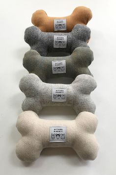 four bone shaped dog toys are lined up on a white surface, one is brown and the other is grey