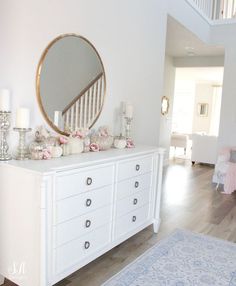 a white dresser topped with lots of drawers next to a mirror and candle holders on top of it