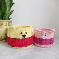 three crocheted baskets with faces on them next to a potted snake plant