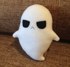 a white stuffed ghost sitting on top of a brown couch next to a black eye patch