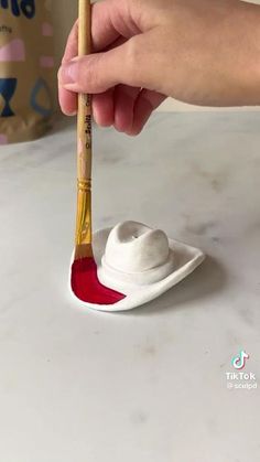 a hand holding a paint brush over a small white plate with a red substance on it