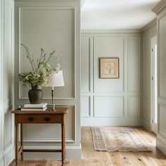 a table with a lamp and flowers on it in a room that has white paneled walls