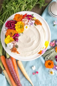 carrots, celery, and flowers are arranged around a cake on a plate