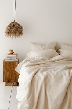 a bed with white linens and pillows in a minimalistic bedroom setting, including a hanging lamp