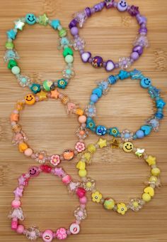 four bracelets with different colored beads and smiley faces on them, sitting on a wooden surface