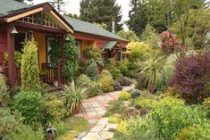 a red house surrounded by lots of trees and plants in front of it, with a stone pathway leading to the door