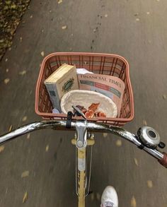 a bicycle with a basket full of food on the handlebars and someone's feet in white shoes